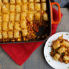 A casserole dish of Tater Tot hotdish with a serving on a plate, showcasing the layers of meat, vegetables, and crispy tater tots.