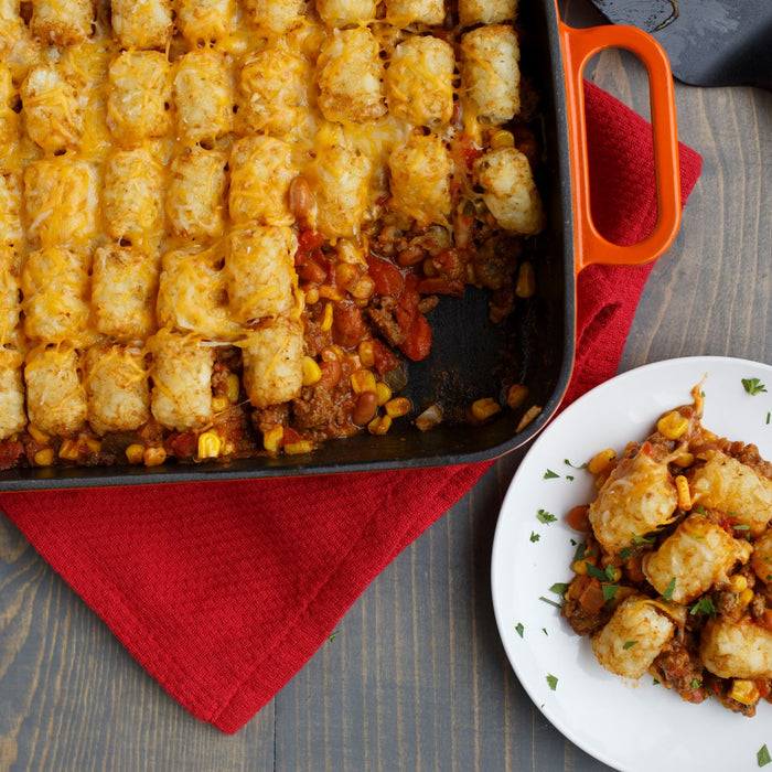 A casserole dish of Tater Tot hotdish with a serving on a plate, showcasing the layers of meat, vegetables, and crispy tater tots.