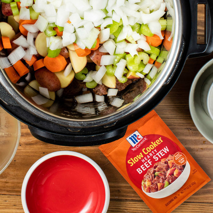 An Instant Pot filled with beef stew ingredients and a McCormick Slow Cookers Beef Stew seasoning packet are displayed on a wooden surface.