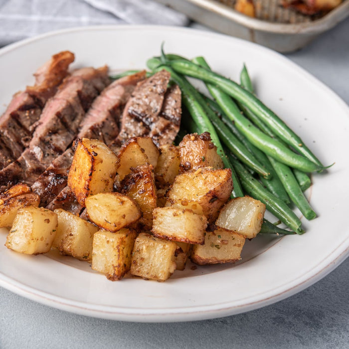 A white plate holds a delicious meal of sliced steak, green beans, and roasted potatoes that have been seasoned with Mccormick Toasted Onion And Garlic Seasoning Mix 1.25 Oz.