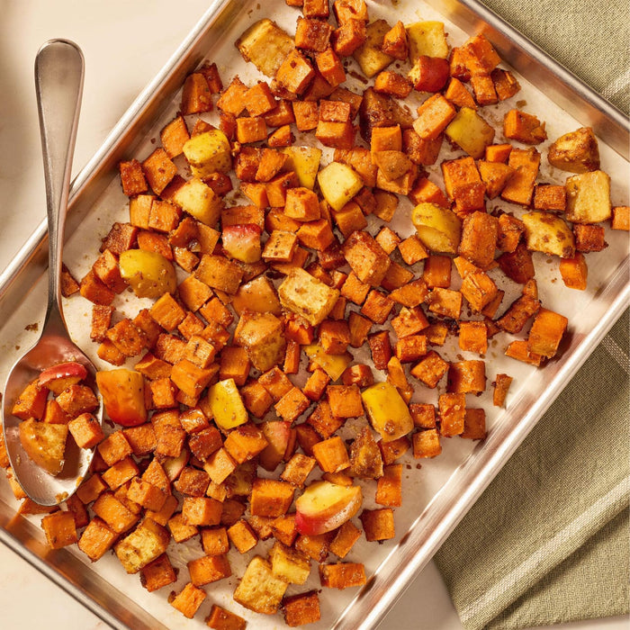 A baking sheet holds roasted sweet potatoes and apples, seasoned to perfection with Mccormick Toasted Onion And Garlic Seasoning Mix 1.25 Oz, with a serving spoon ready to dish them out.
