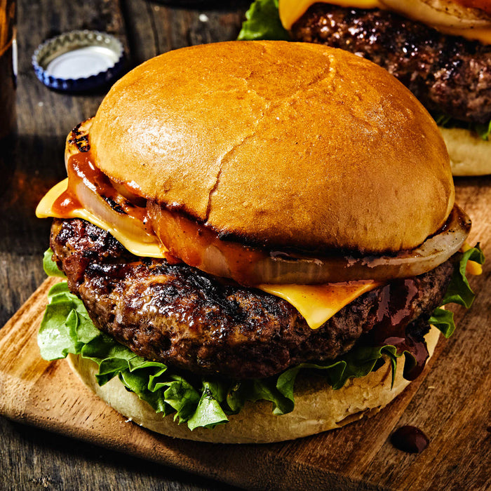 A juicy cheeseburger with lettuce and onion on a wooden cutting board.