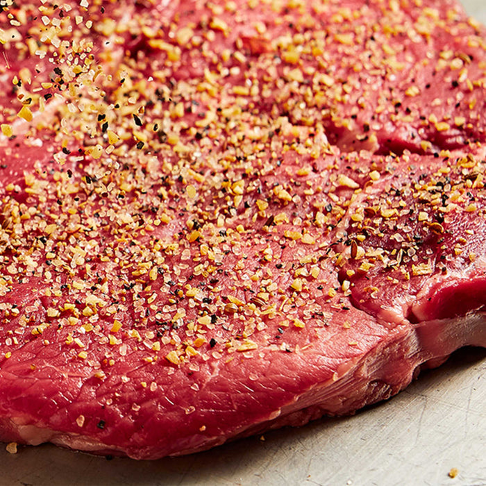 A raw steak seasoned with pepper and spices is ready to be cooked.