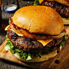 A delicious burger with cheese, lettuce, and grilled onions sits on a wooden board, suggesting a hearty and satisfying meal.