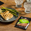 A plate of grilled fish and asparagus with a McCormick Mojito Lime seasoning packet next to it.