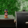 A bottle of Grill Mates Smokehouse Maple seasoning sits on a grill.