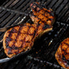 A close-up shows pork chops being grilled on a barbecue, with tongs holding one of the chops.