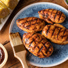 Grilled chicken breasts with barbecue sauce are served on a blue plate with corn on the cob.