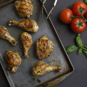 Grilled chicken pieces are arranged on a metal tray alongside fresh tomatoes and basil.