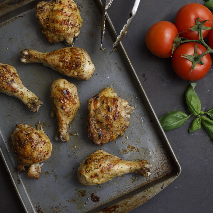 Grilled chicken pieces are arranged on a metal tray alongside fresh tomatoes and basil.