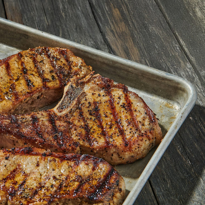 Grilled pork chops with visible grill marks are arranged on a metal tray.