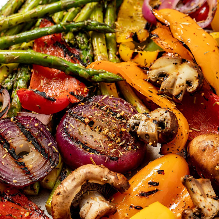 A close-up shot of grilled vegetables including asparagus red and yellow peppers red onions and mushrooms seasoned with herbs.