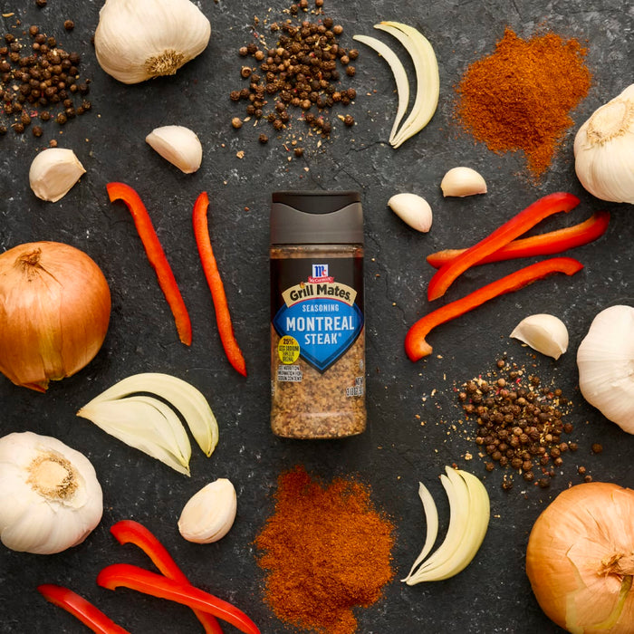 A bottle of McCormick Montreal Steak Spice is surrounded by fresh ingredients like garlic, onions, red peppers, and spices, suggesting its use in cooking.
