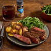 A plate of steak seasoned with McCormick Grill Mates Montreal Steak Seasoning, served with potatoes and salad, alongside a glass of iced tea.