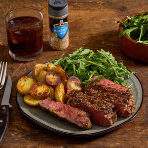 A plate of steak seasoned with McCormick Grill Mates Montreal Steak Seasoning, served with potatoes and salad, alongside a glass of iced tea.