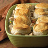 A green casserole dish filled with chicken pot pie with biscuits on top.