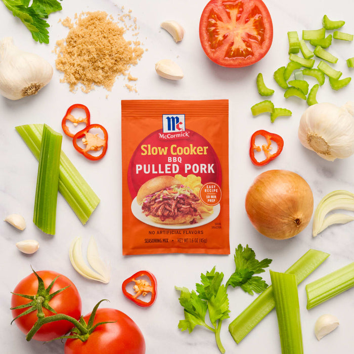 McCormick Slow Cooker Pulled Pork seasoning packet surrounded by fresh ingredients like tomatoes, celery, garlic, and onion.