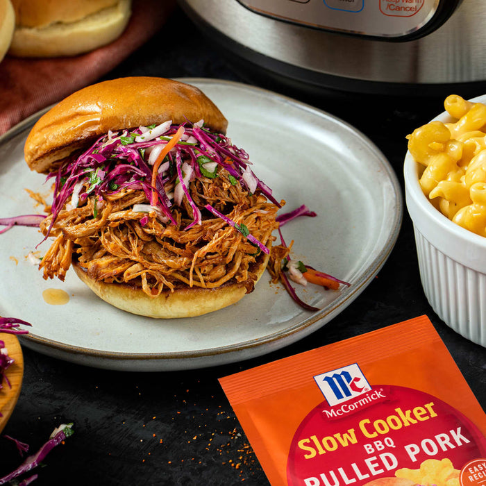 A pulled pork sandwich with McCormick Slow Cooker Pulled Pork seasoning is served with mac and cheese.
