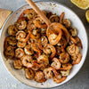 A white pan with a wooden spoon in it filled with cooked shrimp and spices.