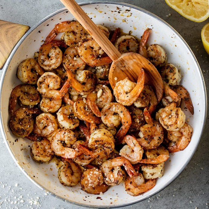 A white pan with a wooden spoon in it filled with cooked shrimp and spices.
