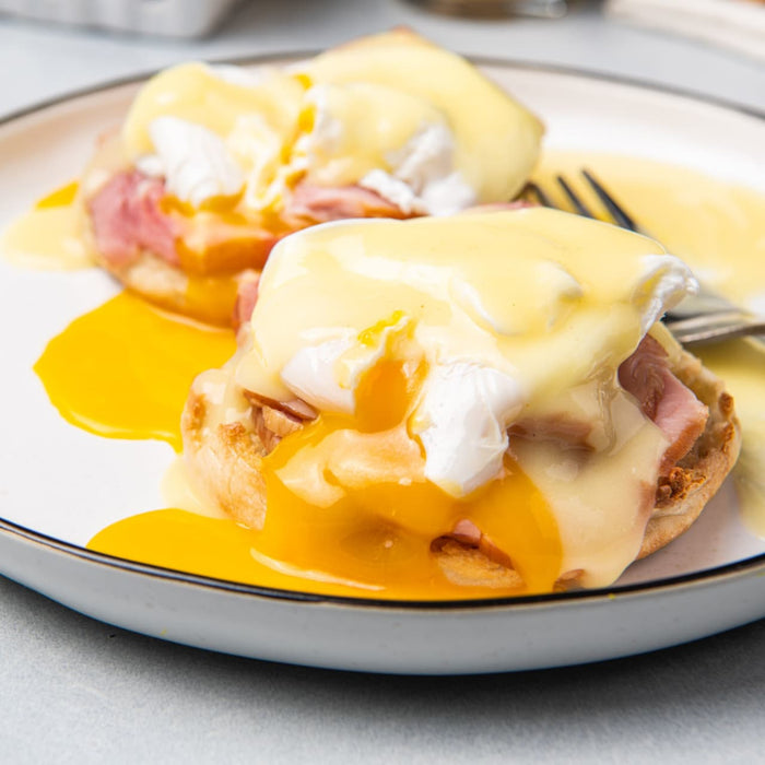 Two eggs benedict with ham on english muffins covered in hollandaise sauce.