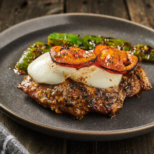 A plate of grilled chicken topped with mozzarella and tomato slices accompanied by grilled green peppers.