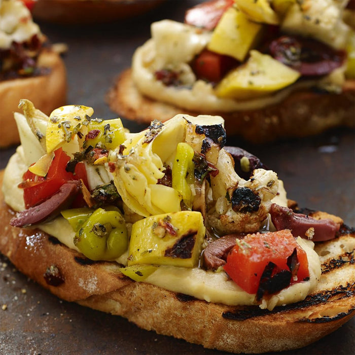 A close-up shot of a bruschetta topped with grilled vegetables and herbs.