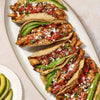 Several chicken tacos, prepared with Mccormick Chicken Taco Seasoning Mix, are neatly arranged on a white platter, generously filled with seasoned chicken, fresh avocado slices, diced tomatoes, red onions, and crumbled white cheese.