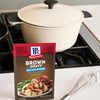 A packet of McCormick Brown Gravy mix sits next to a pot and whisk on a stovetop.