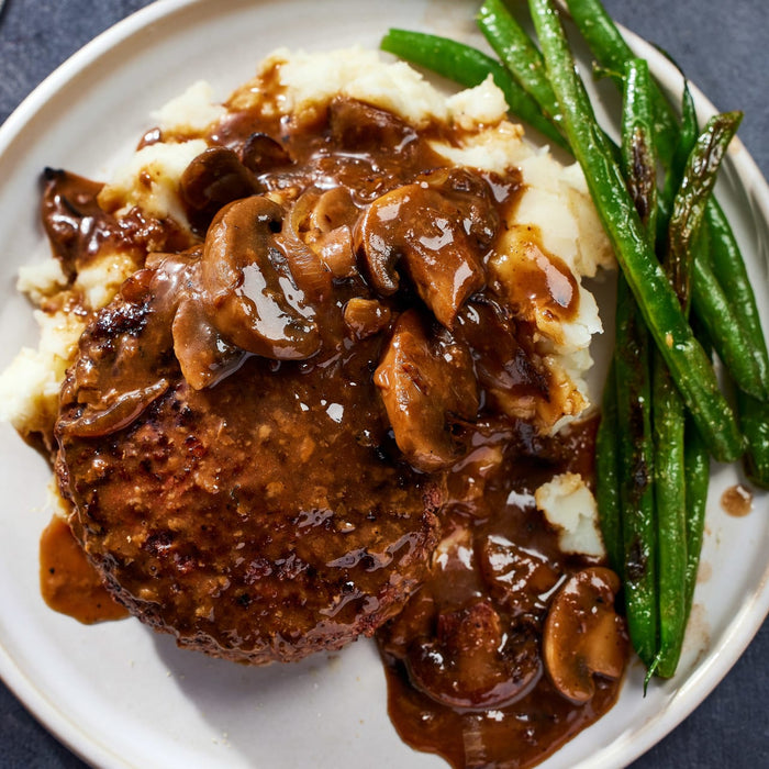 A plate of Salisbury steak with mushroom gravy, mashed potatoes, and green beans.