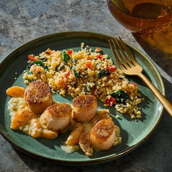 A plate of seared scallops served with a colorful couscous salad and a creamy sauce.