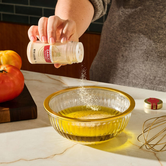 A person is adding McCormick garlic powder to a bowl of olive oil, likely preparing a salad dressing.