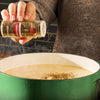 A person adds McCormick Italian Herb Seasoning to a pot of simmering liquid.