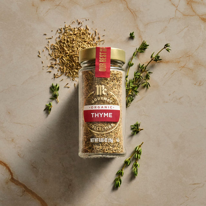 A jar of Thyme spice from The Spice Hunter brand is displayed with loose thyme and fresh thyme sprigs on a marble surface.