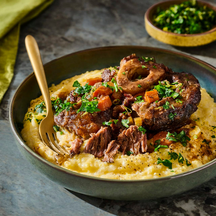 A hearty plate of osso buco served over creamy polenta, garnished with fresh herbs.