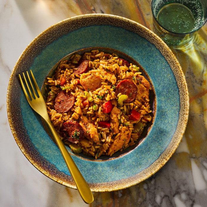 A bowl of jambalaya with sausage and chicken is presented on a blue plate with a gold fork.
