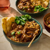 A bowl of rich, flavorful beef curry served with rice and naan bread, garnished with fresh cilantro.