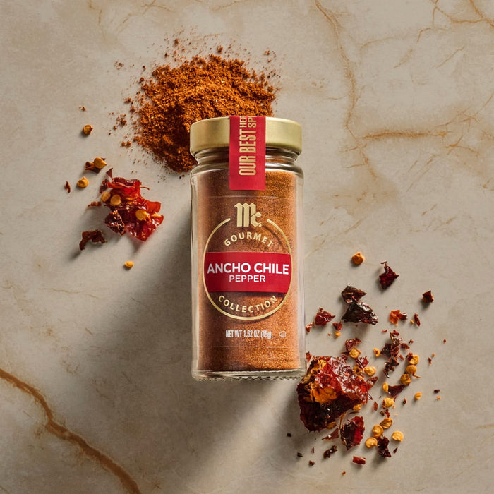 A jar of McCormick Ancho Chile Pepper is displayed with a pile of the spice and chili flakes on a marble surface.