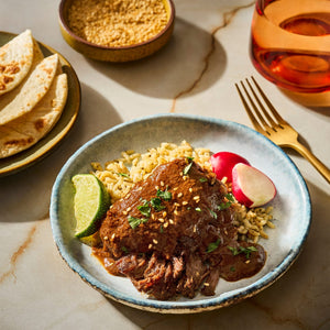 A flavorful dish featuring braised meat in a rich sauce, served with rice, radishes, and a lime wedge, accompanied by tortillas.