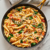 A pan of penne pasta with chicken spinach and tomatoes topped with shredded cheese.