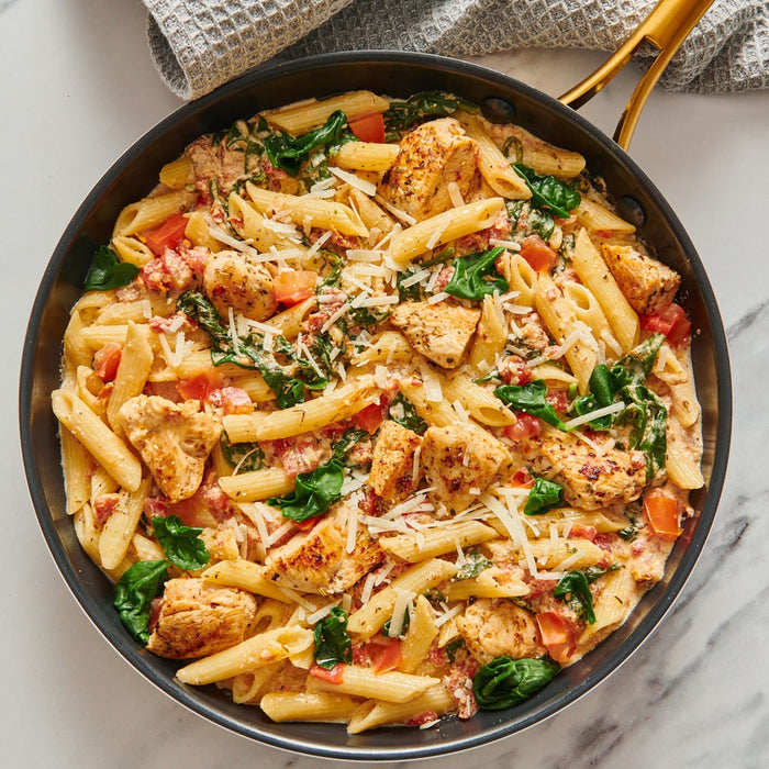A pan of penne pasta with chicken spinach and tomatoes topped with shredded cheese.