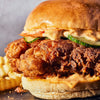 A delicious fried chicken sandwich with sauce, pickles, and fries.