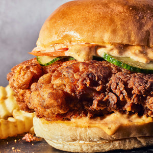 A delicious fried chicken sandwich with sauce, pickles, and fries.