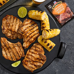 A plate featuring grilled pork chops seasoned with Grill Mates Chipotle Pepper seasoning, alongside grilled corn and lime wedges.