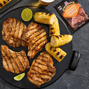 A plate featuring grilled pork chops seasoned with Grill Mates Chipotle Pepper seasoning, alongside grilled corn and lime wedges.