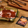 A person pours sauce over pork chops in a glass baking dish, with a McCormick Chipotle Pepper seasoning packet nearby.
