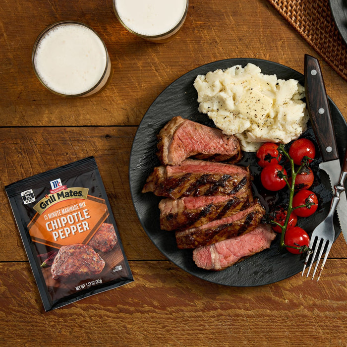 A plate of grilled steak with McCormick Montreal Steak Spice seasoning, served with mashed potatoes and tomatoes, accompanied by two glasses of beer.