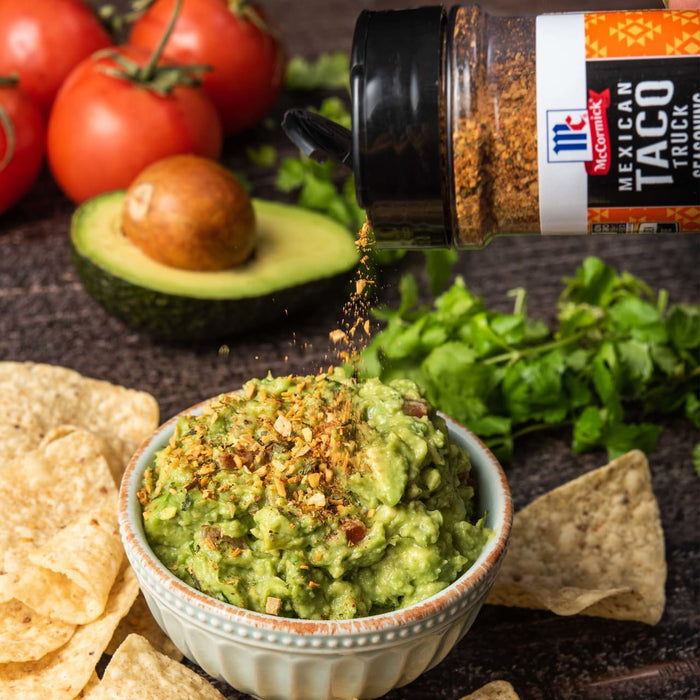 A bowl of guacamole with tortilla chips and McCormick Mexican Taco Truck seasoning being sprinkled on top.