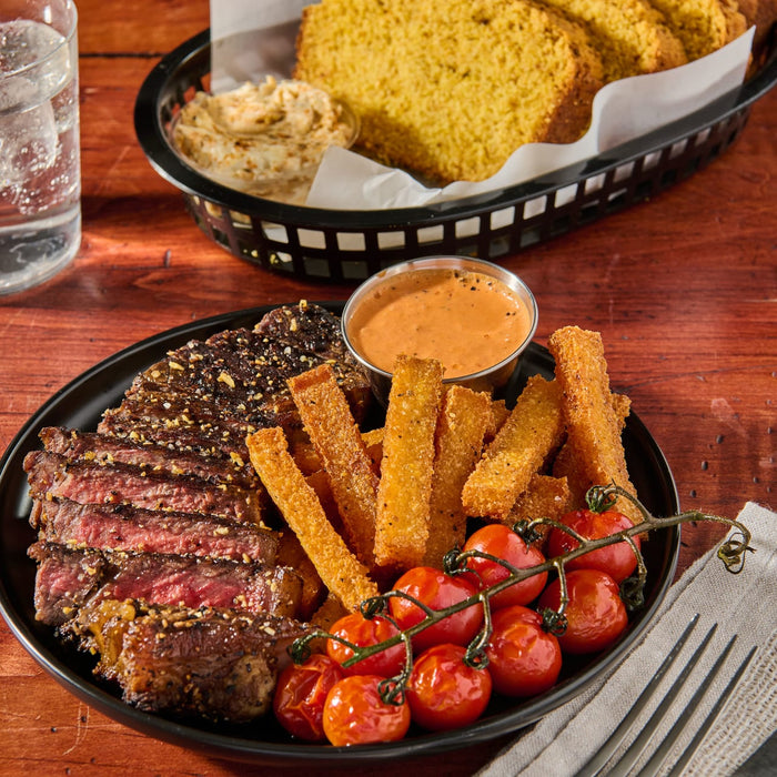 A plate of steak cornbread fries cherry tomatoes and a side of dipping sauce.
