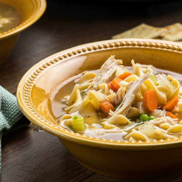 A bowl of chicken noodle soup with carrots, peas, and celery.